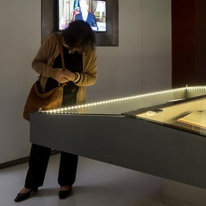 Visitante consulta a vitrina com documentação relativa aos poderes do Presidente da República; à esquerda, um vídeo sintetiza os poderes e funções do Presidente.