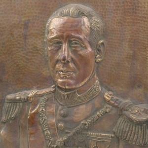 Baixo-relevo em cobre dourado com a representação do busto do Presidente Francisco Craveiro Lopes. Peça com 40 cm de altura por 29,5 cm de largura por 2,5 cm de espessura.