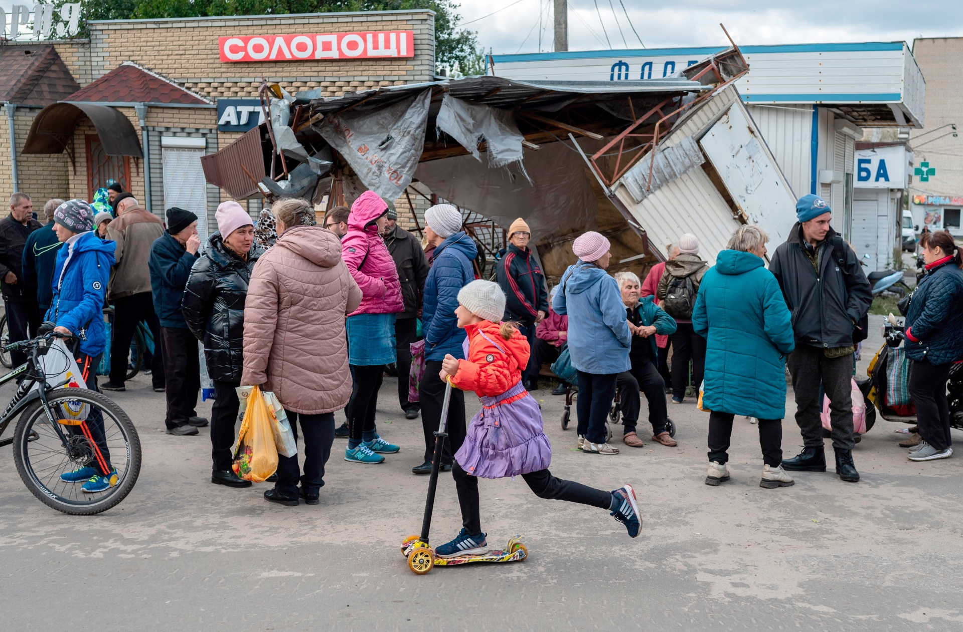 Lera (10 anos) anda de trotineta junto a uma fila para ajuda humanitária, na cidade recentemente libertada de Izium.